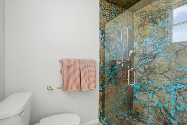 Glass-enclosed shower with unique stone-patterned tile, herringbone mosaic shower surround, and a chrome shower head
