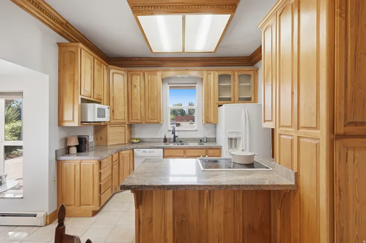 Wood-finish cabinetry, light-toned countertops, tile flooring, and integrated cooktop
