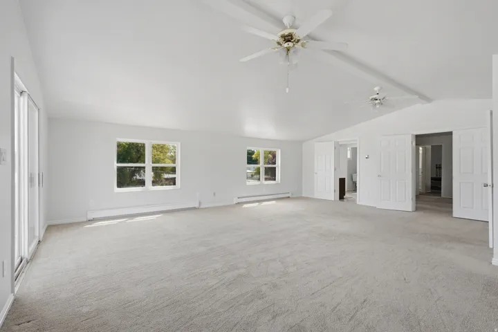 Vaulted ceilings, dual ceiling fans, light gray carpeting, sliding glass door, and multiple windows