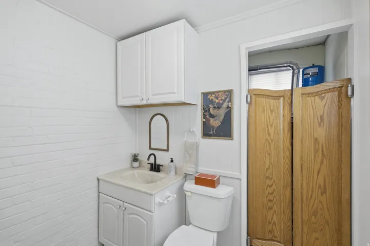 White painted brick wall, vanity with integrated sink, matte black faucet, wall-mounted upper cabinetry, and wood-finish saloon doors