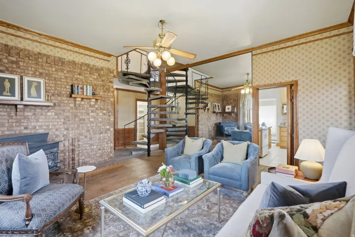 Exposed brick wall, spiraling staircase, wood-finish flooring, ceiling fan, and ornate wall paneling