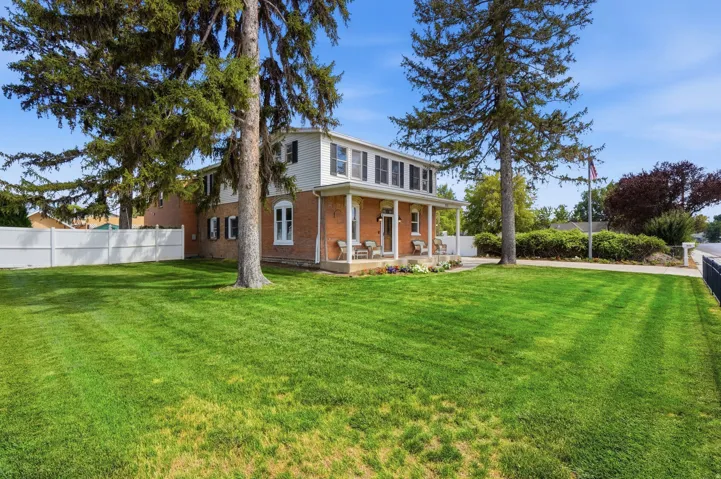 Brick exterior with white trim, covered front porch, expansive lawn, and mature trees