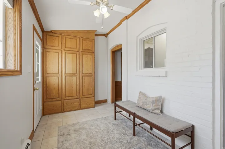 Built-in wood cabinetry, tiled flooring, ceiling fan, and white painted brick wall