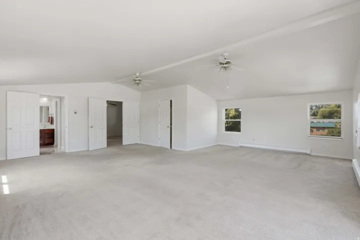 Spacious room featuring vaulted ceilings, light-colored carpeting, two ceiling fans, and multiple windows