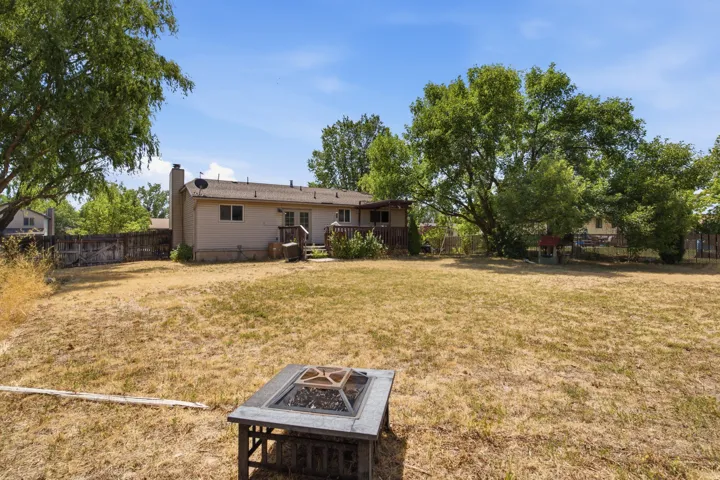 Expansive backyard with mature trees, a fire pit, and a wooden deck