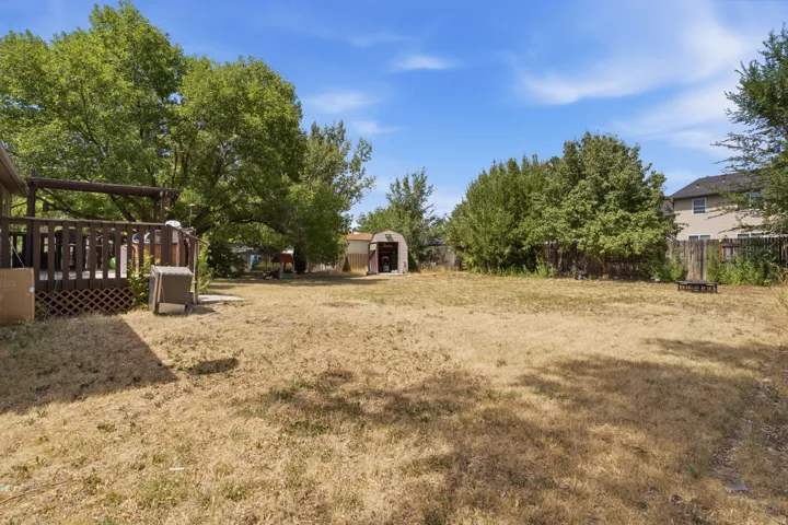 Expansive backyard featuring a wood deck with lattice detailing, mature trees, and a storage shed