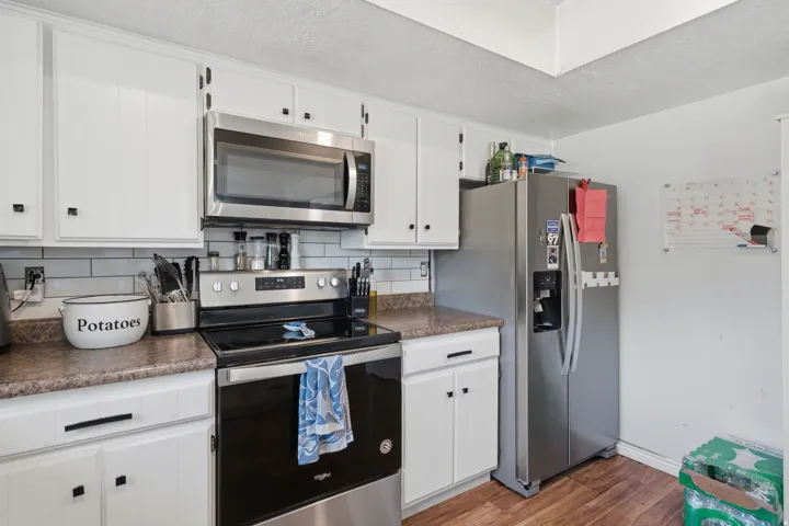 White cabinetry with matte black hardware, stainless steel microwave, electric range, and refrigerator, complemented by a white subway tile backsplash and wood-finish flooring