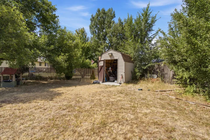 Detached storage shed with a roll-up door, surrounded by mature trees and a wooden fence