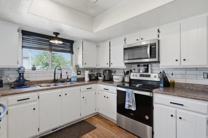 White cabinetry, stainless steel appliances, wood-finish flooring, subway tile backsplash, and dark countertops