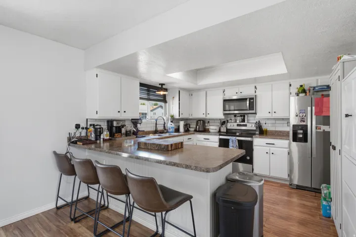 Kitchen featuring white cabinetry, a counter-height island with seating, stainless steel appliances, a subway tile backsplash, and wood-finish flooring