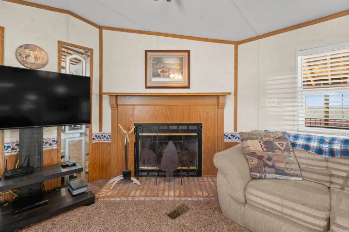 Recessed fireplace with a wood-finish mantel and a brick hearth, window with blinds, and carpeted flooring
