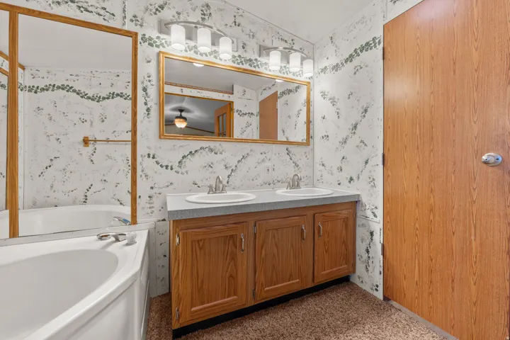 Primary bathroom.  Dual vanity with two sinks, a built-in bathtub, and a wood-finish cabinet