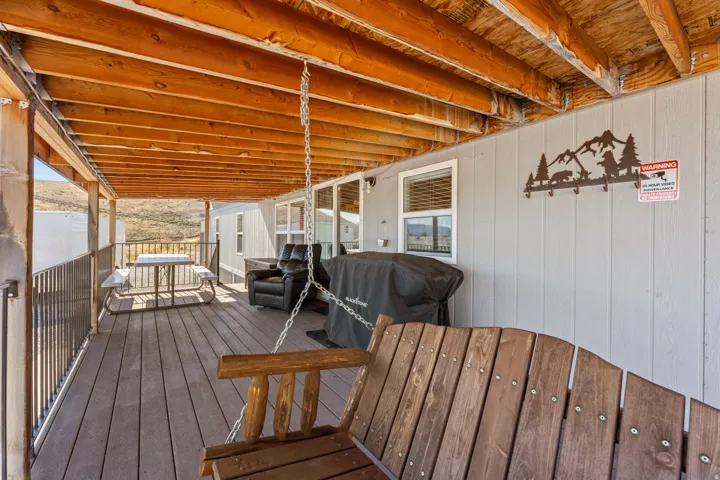 Covered outdoor deck with wood-finish decking, exposed wood beam ceiling, and a dark metal railing