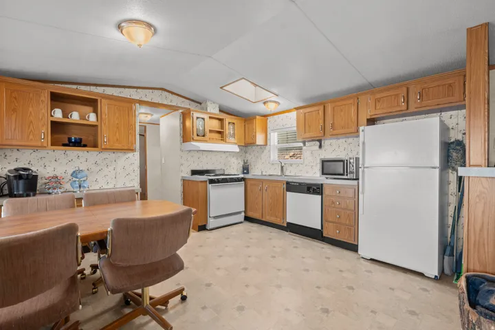 Kitchen with wood-finish cabinetry, white appliances, and a skylight