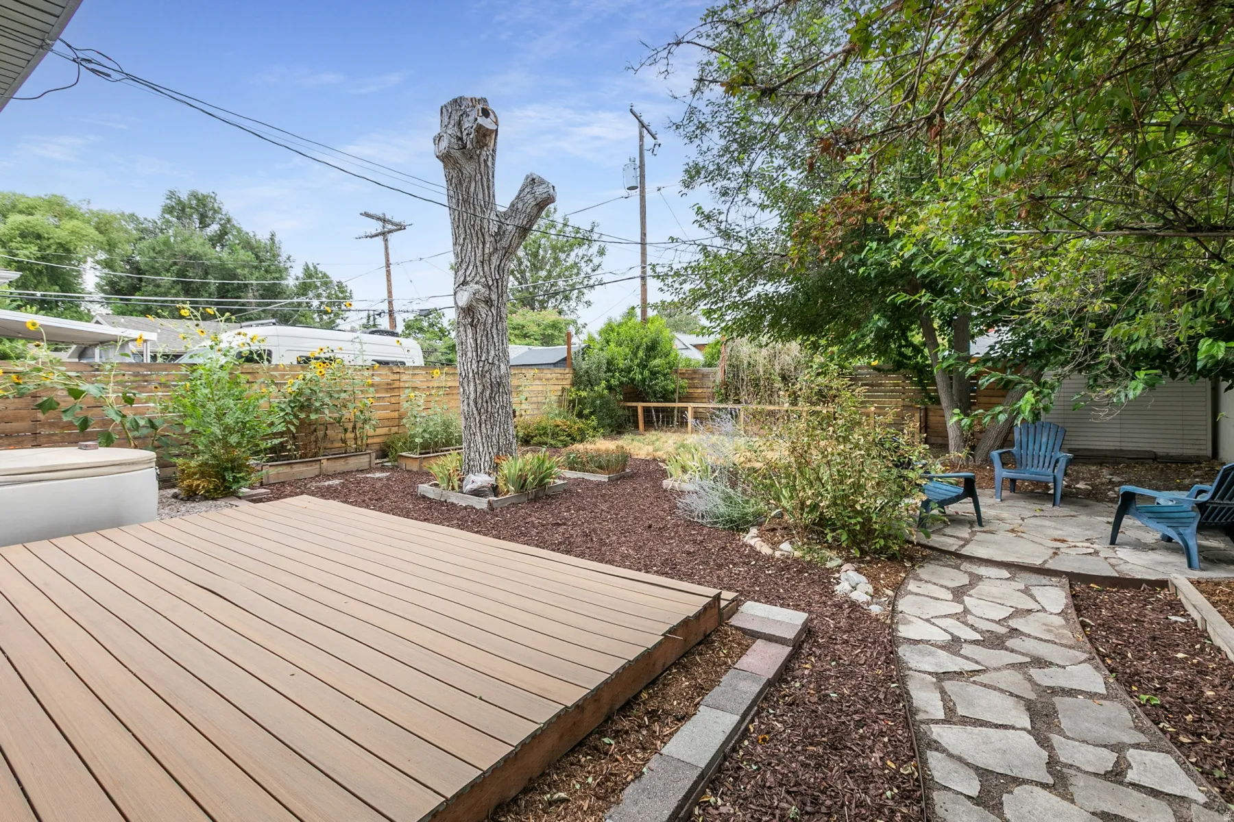 Wood-finish deck with a flagstone path, raised garden beds, and mature trees
