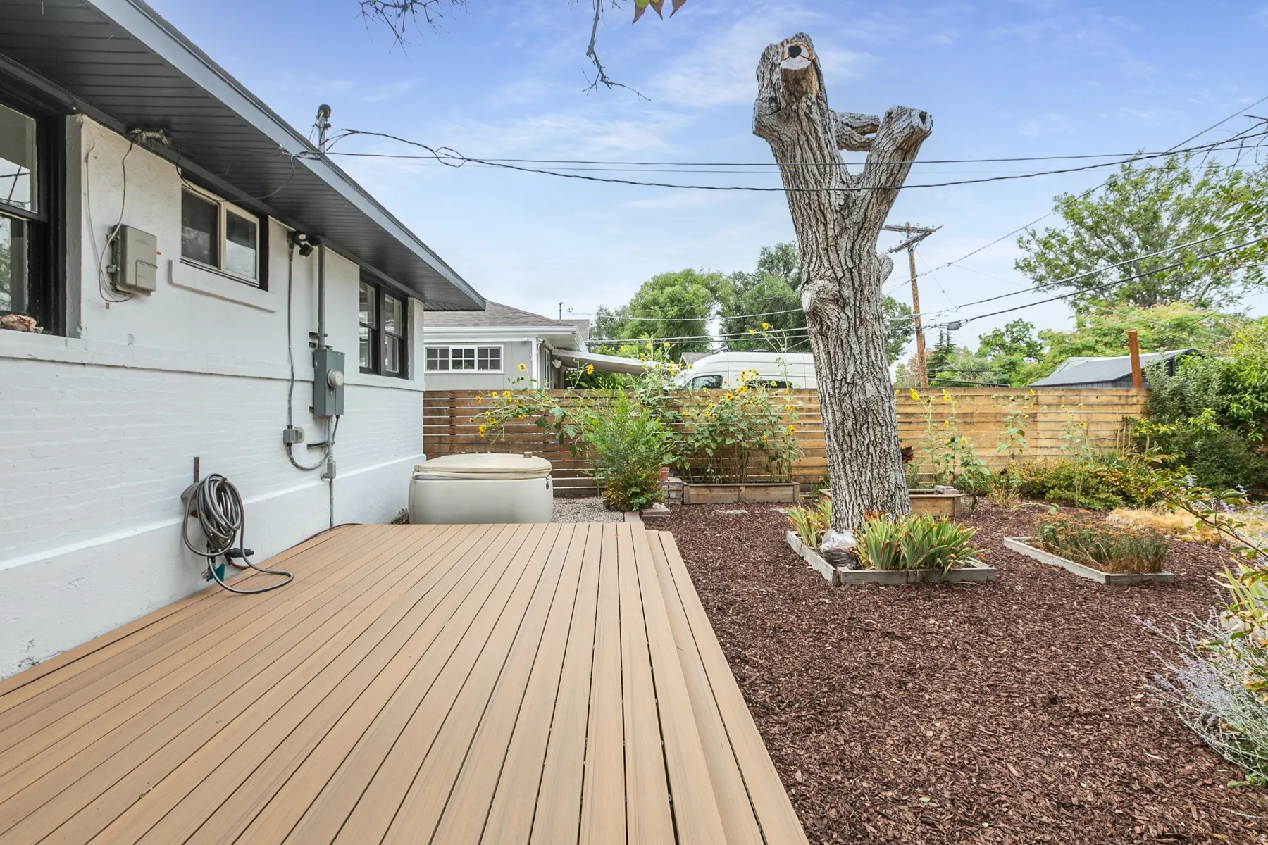 Exterior featuring a composite deck, white brick siding, a privacy fence, and planted garden beds