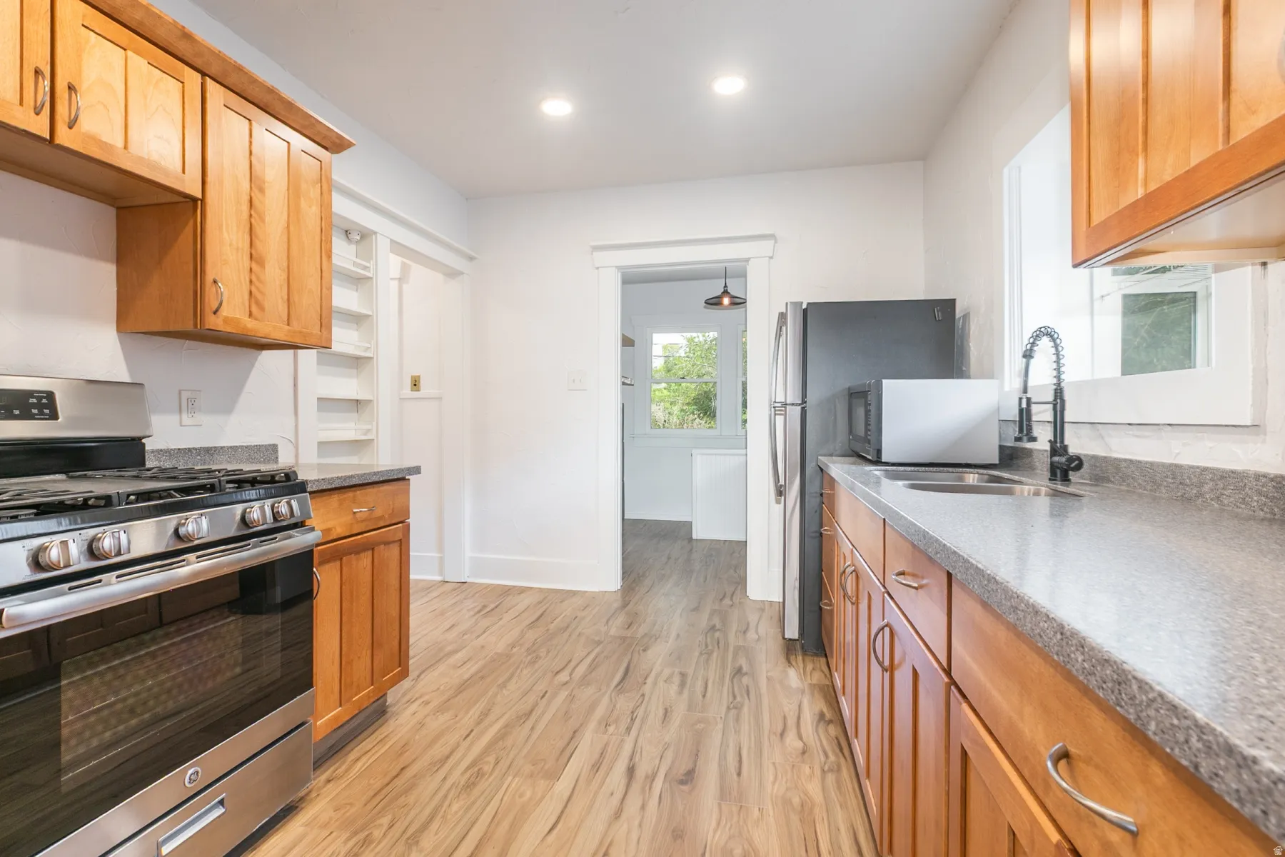 Wood-finish flooring, recessed lighting, wood cabinetry, stainless steel range, and a stainless steel sink with a matte black faucet