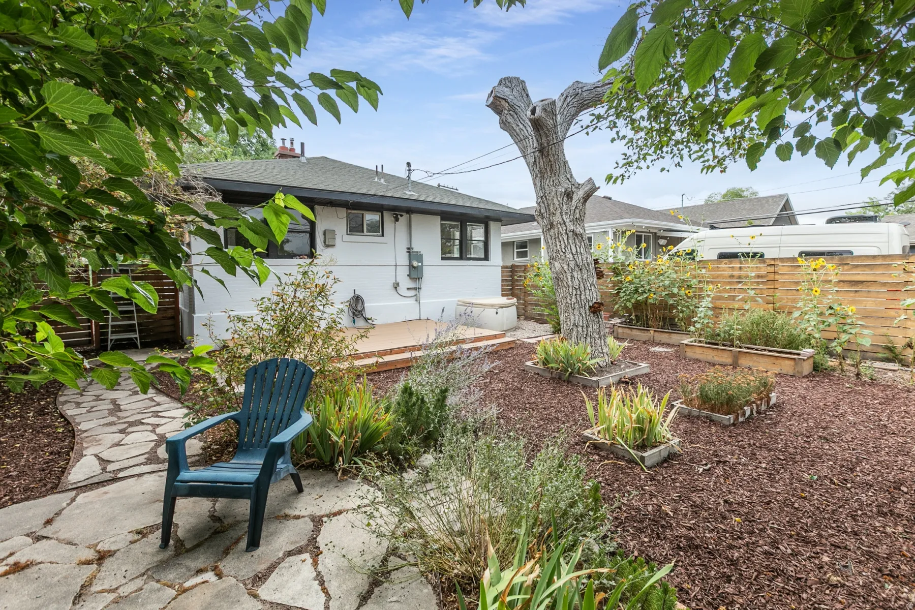 Backyard featuring a flagstone pathway, wood chip ground cover, raised garden beds, and a wood privacy fence