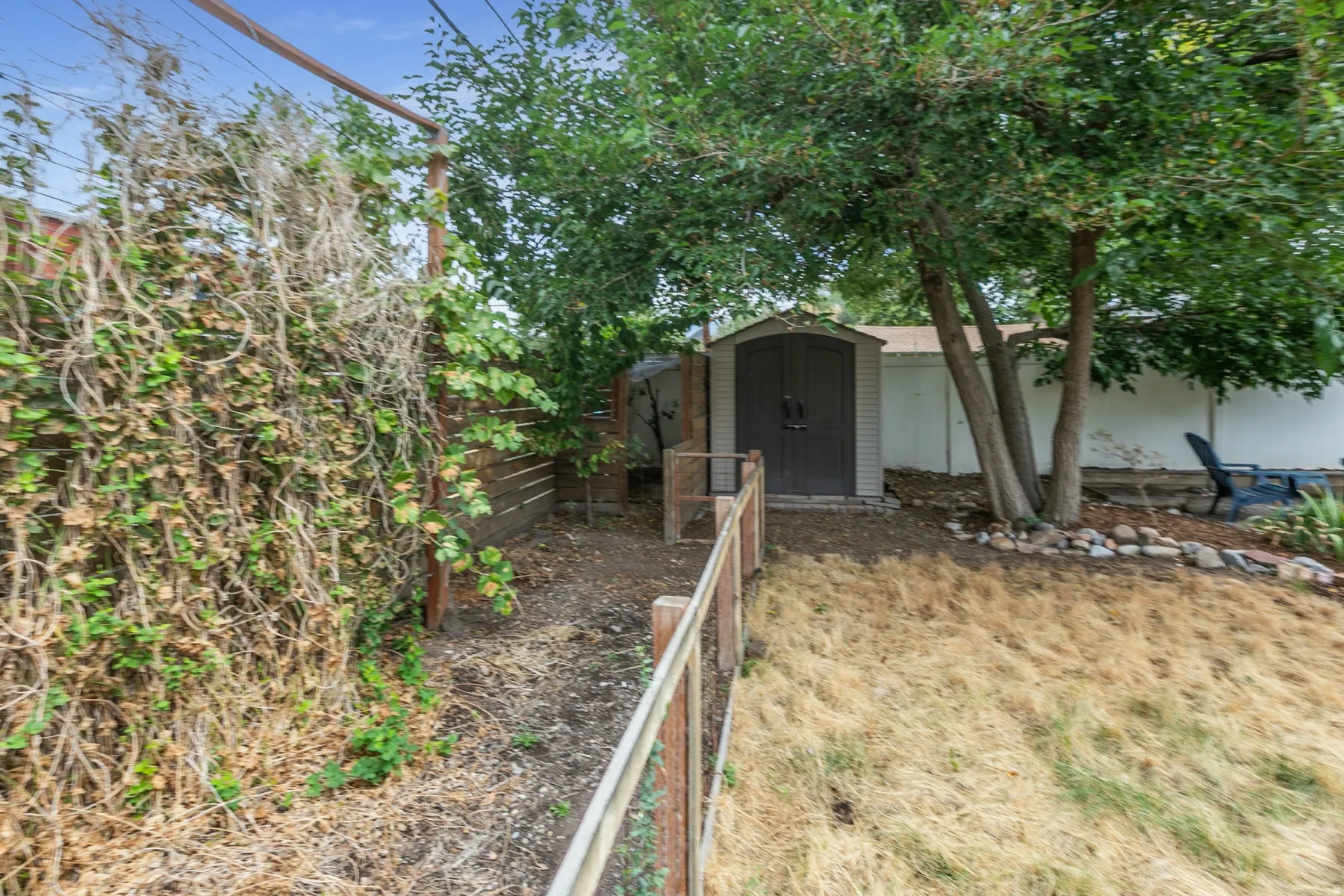 Detached storage shed, mature trees, wood fence, rock landscaping, and wood arbor