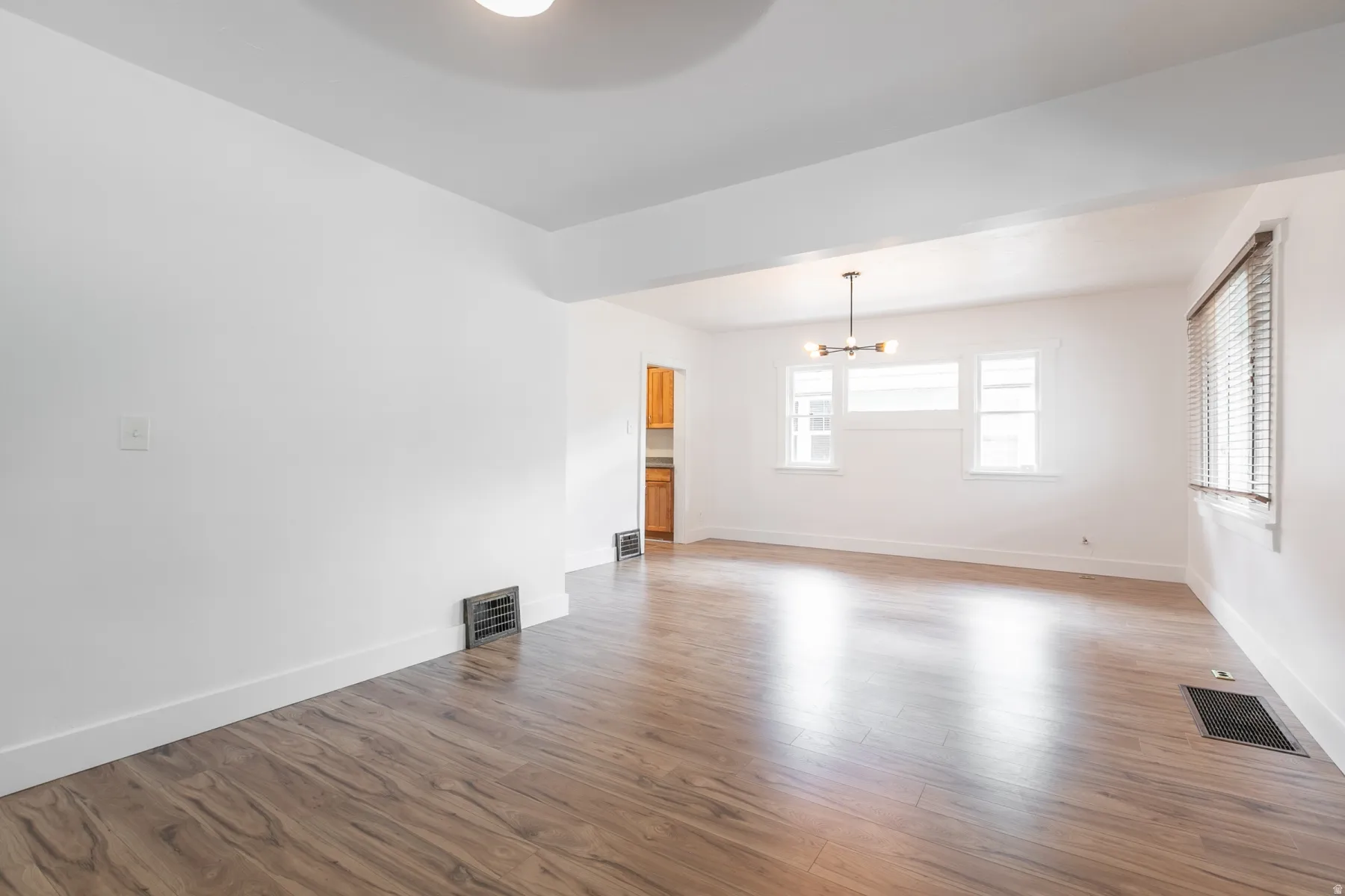 Spacious room with wood-finish flooring, white walls, and multiple windows with blinds
