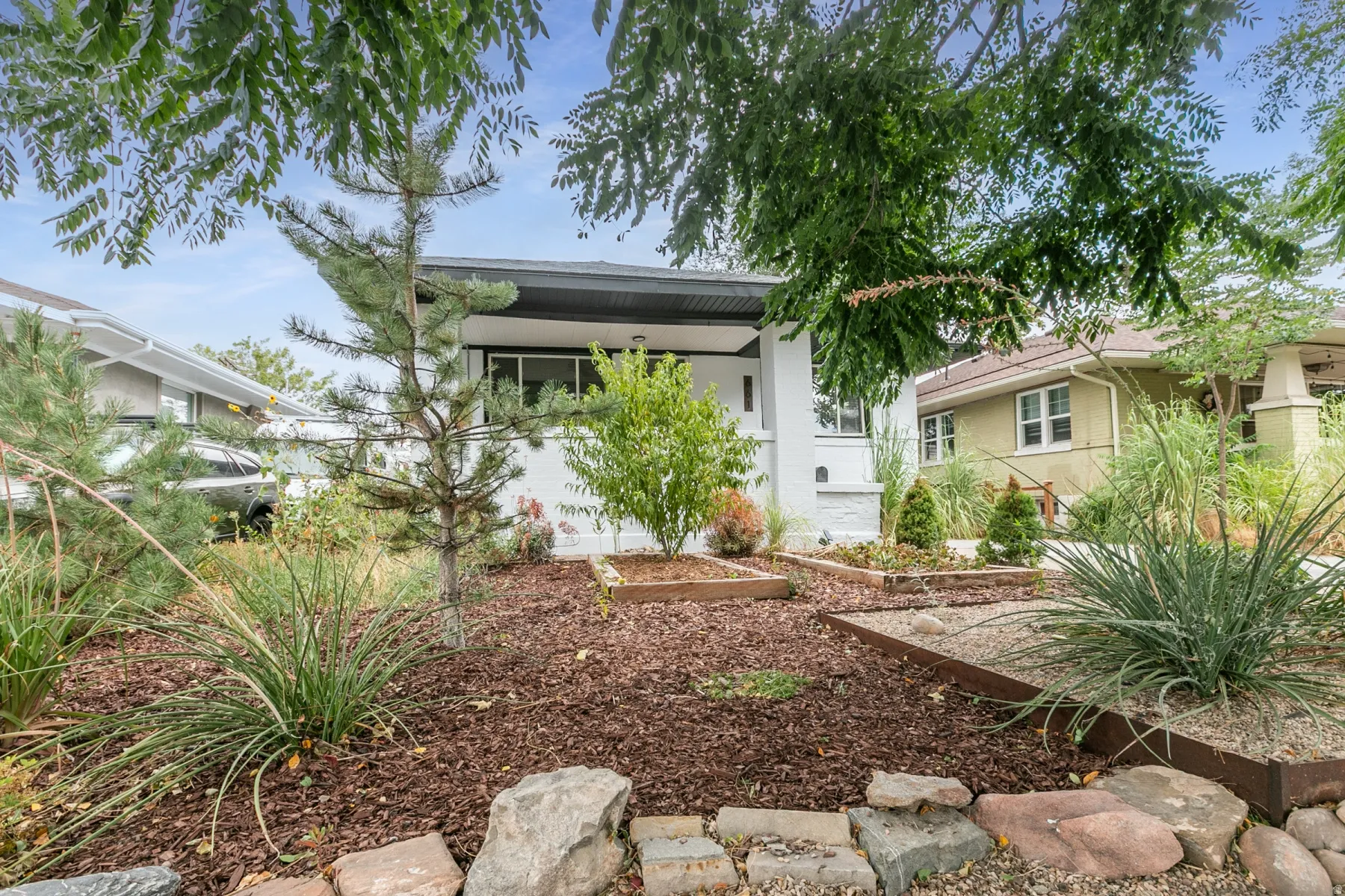 Front yard featuring mature trees, diverse plantings, and garden beds with wood and metal edging