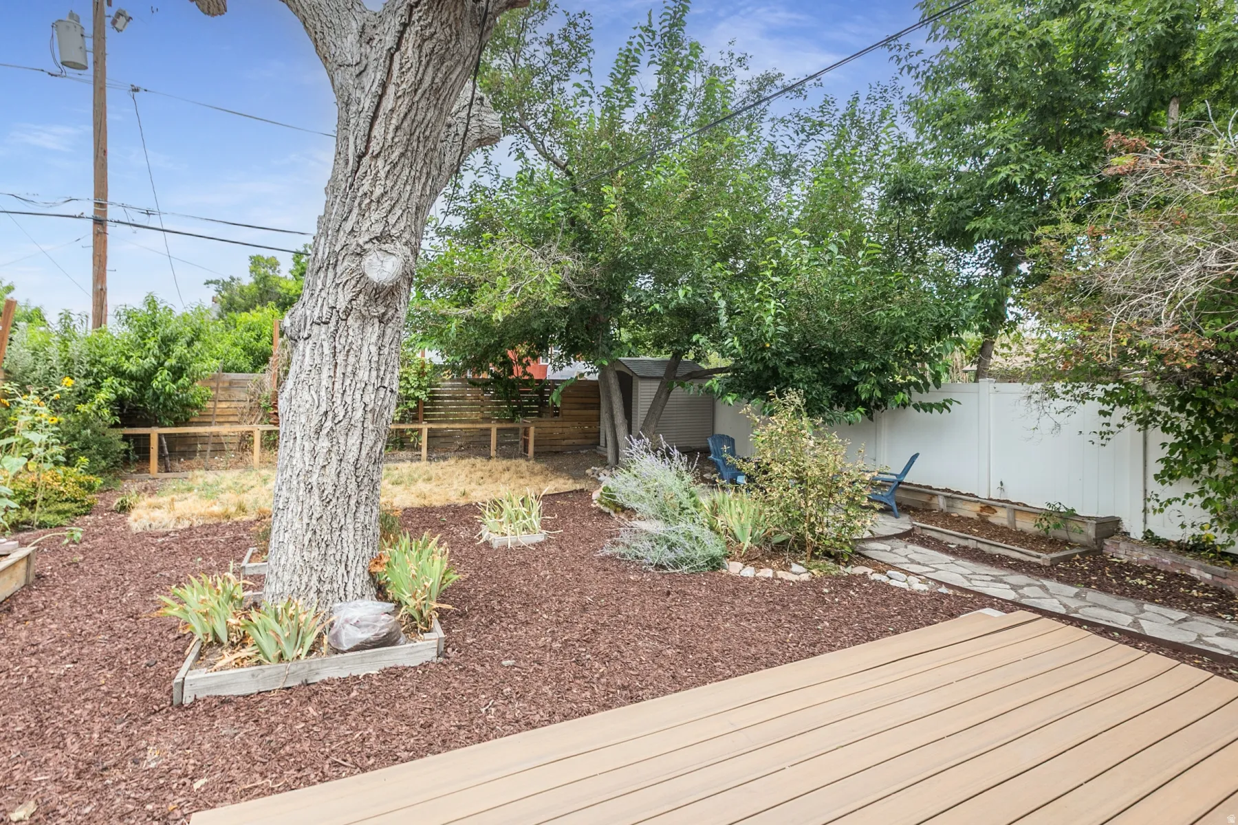 Expansive backyard featuring a composite deck, mature trees, wood chip ground cover, and a stone walkway