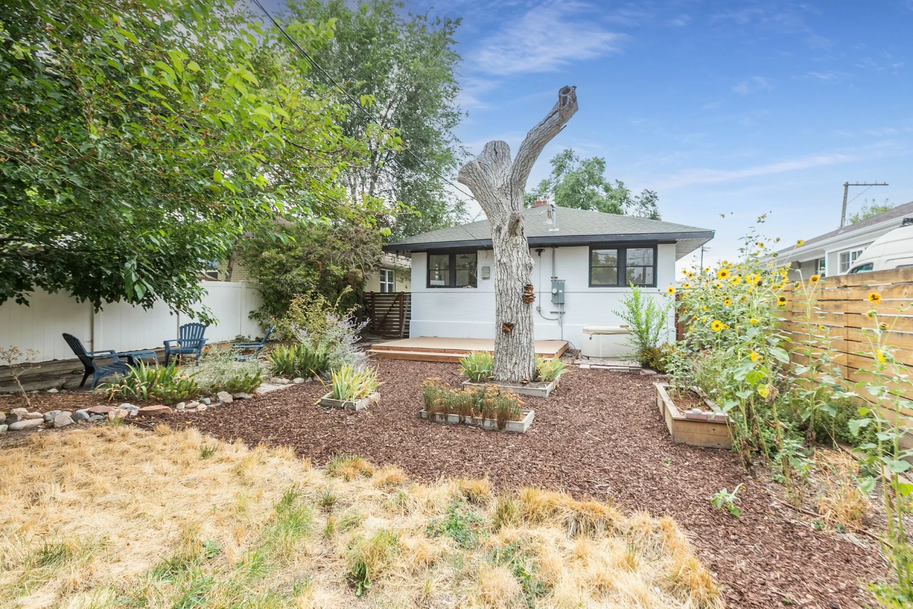 White stucco exterior with black-framed windows, a wood deck, a wood chip ground cover, and a wood fence