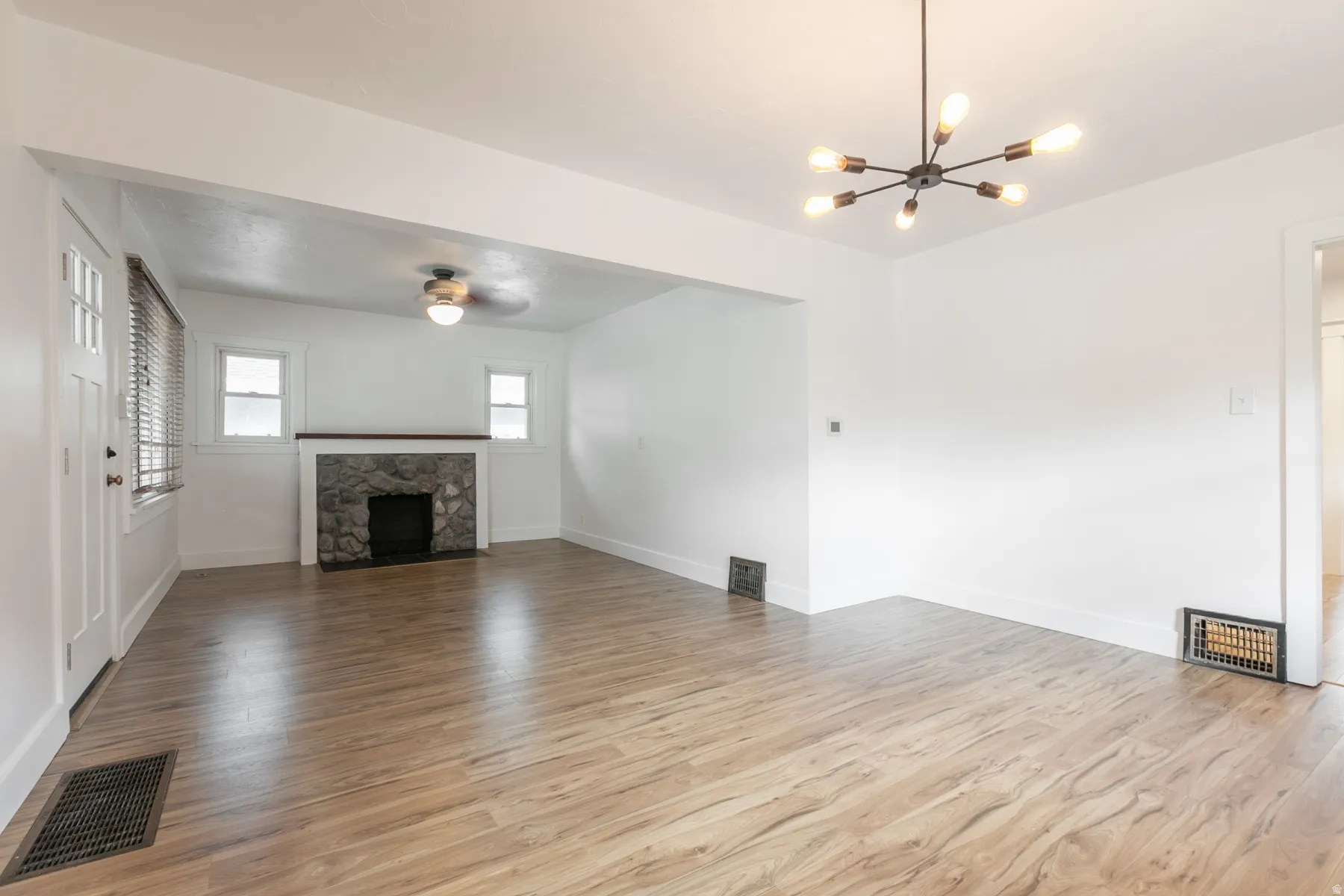 Wood-finish flooring throughout, stone fireplace with a wood mantel, modern black chandelier, and a ceiling fan
