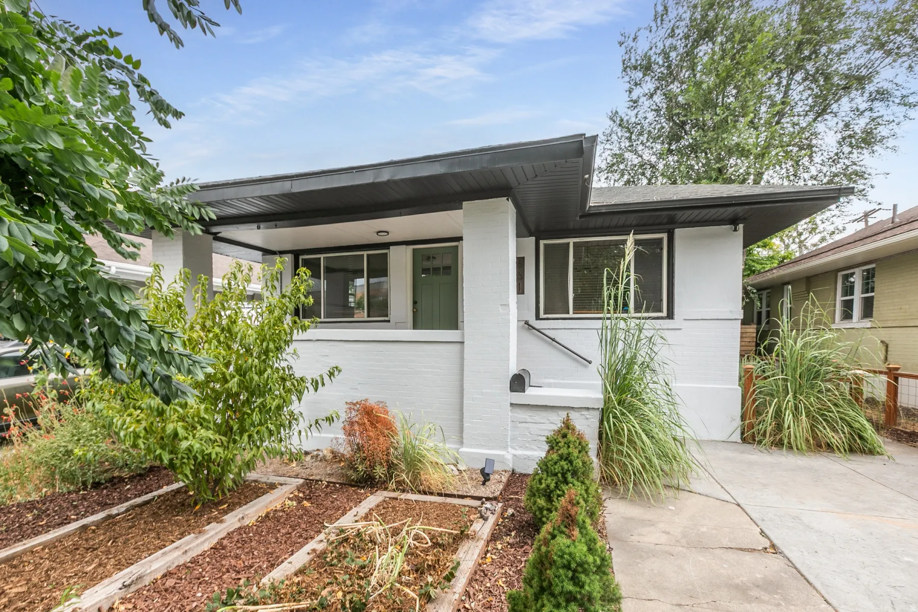 Contemporary residence featuring a light-toned exterior, dark trim, a covered entry, and a paved driveway