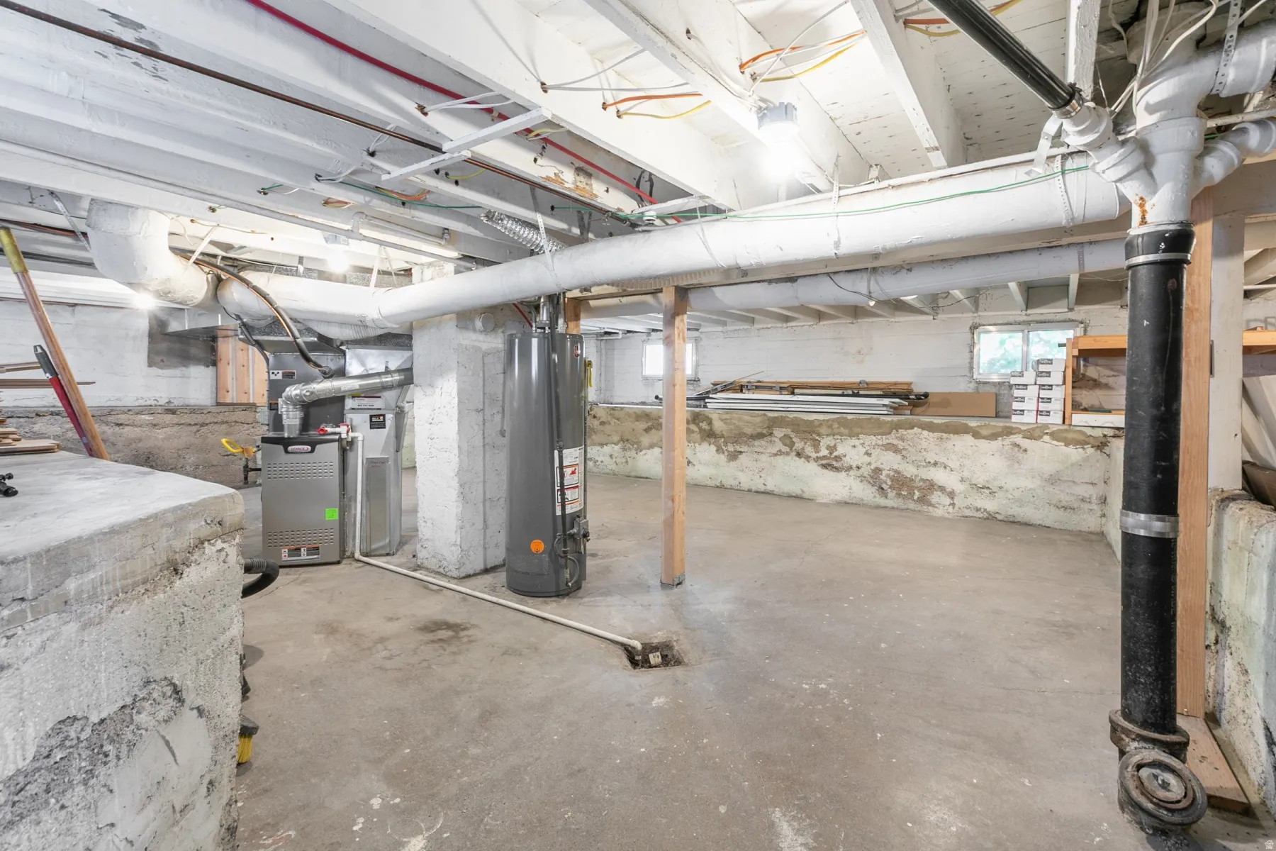 Basement featuring exposed ceiling joists, concrete flooring, a water heater, and a furnace