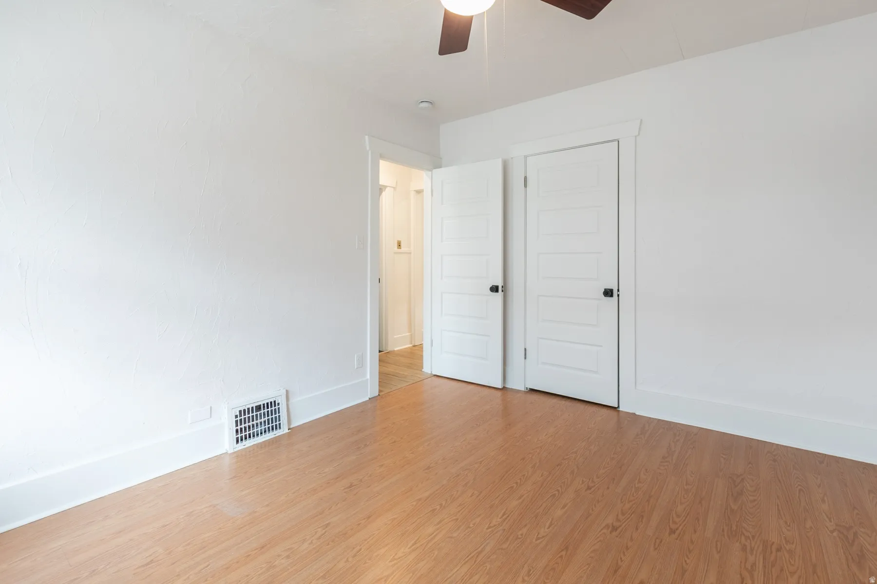 Wood-finish flooring, white paneled doors with black hardware, and a ceiling fan with integrated lighting