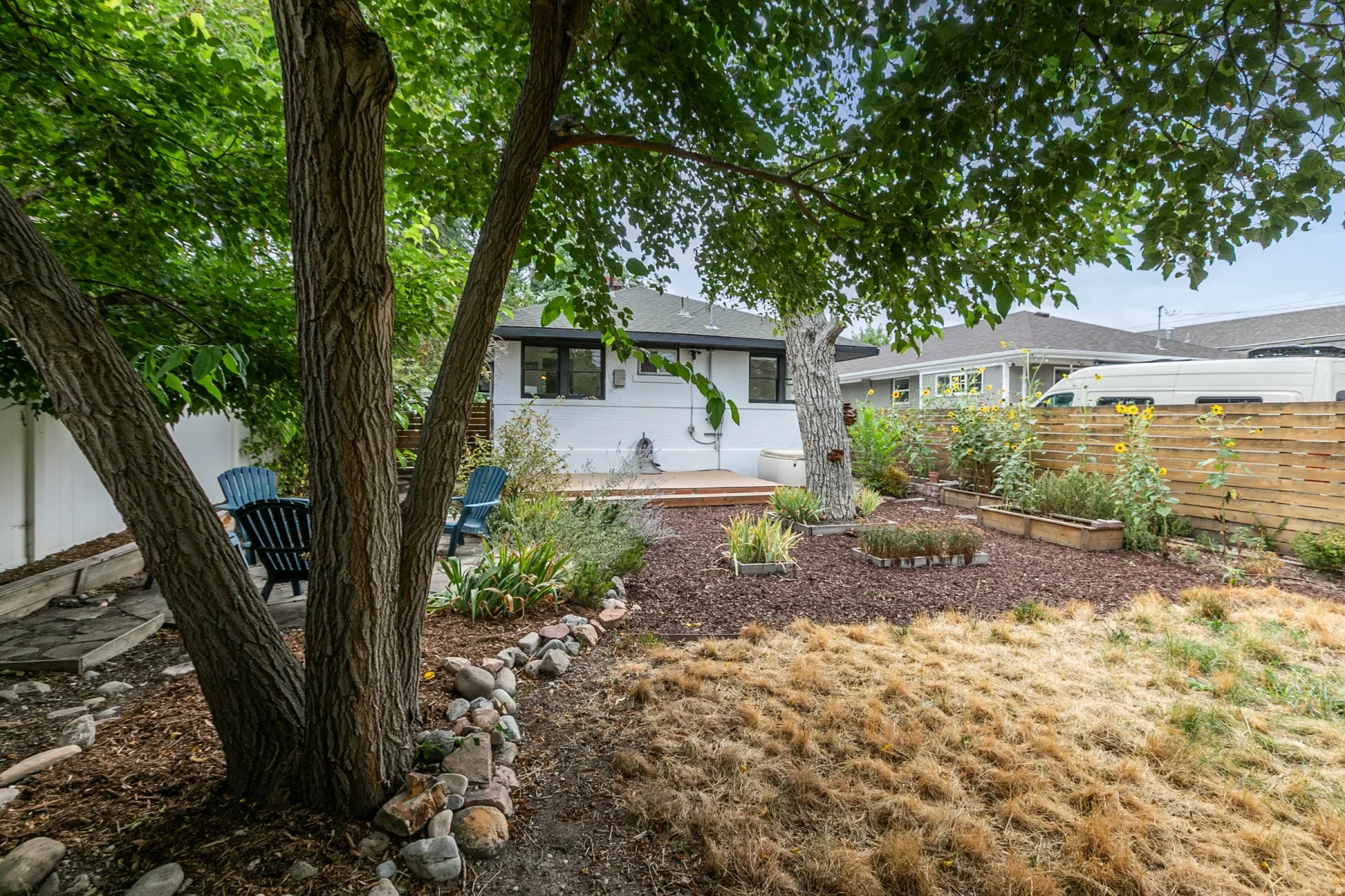Expansive backyard featuring mature trees, wood decking, a rock-lined garden bed, and a privacy fence