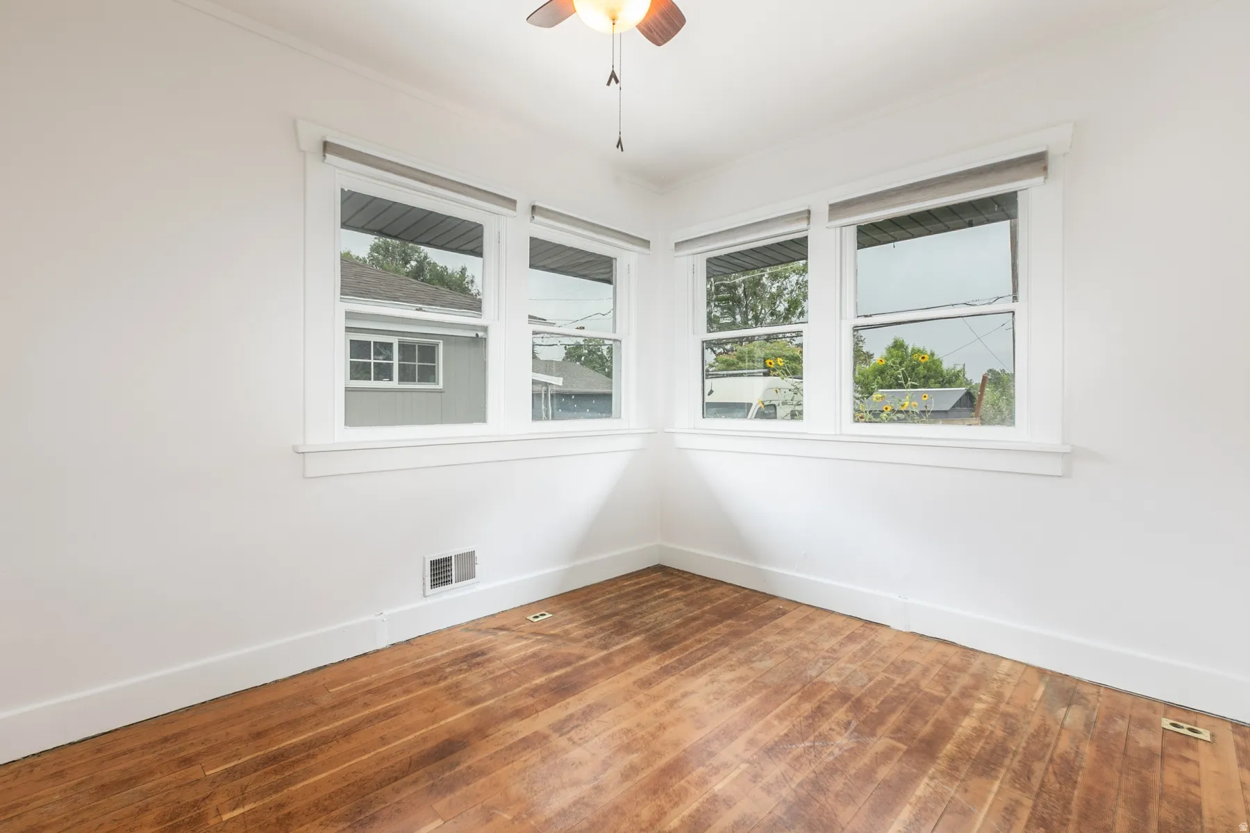 Hardwood flooring, corner window configuration, white trim, white walls, ceiling fan