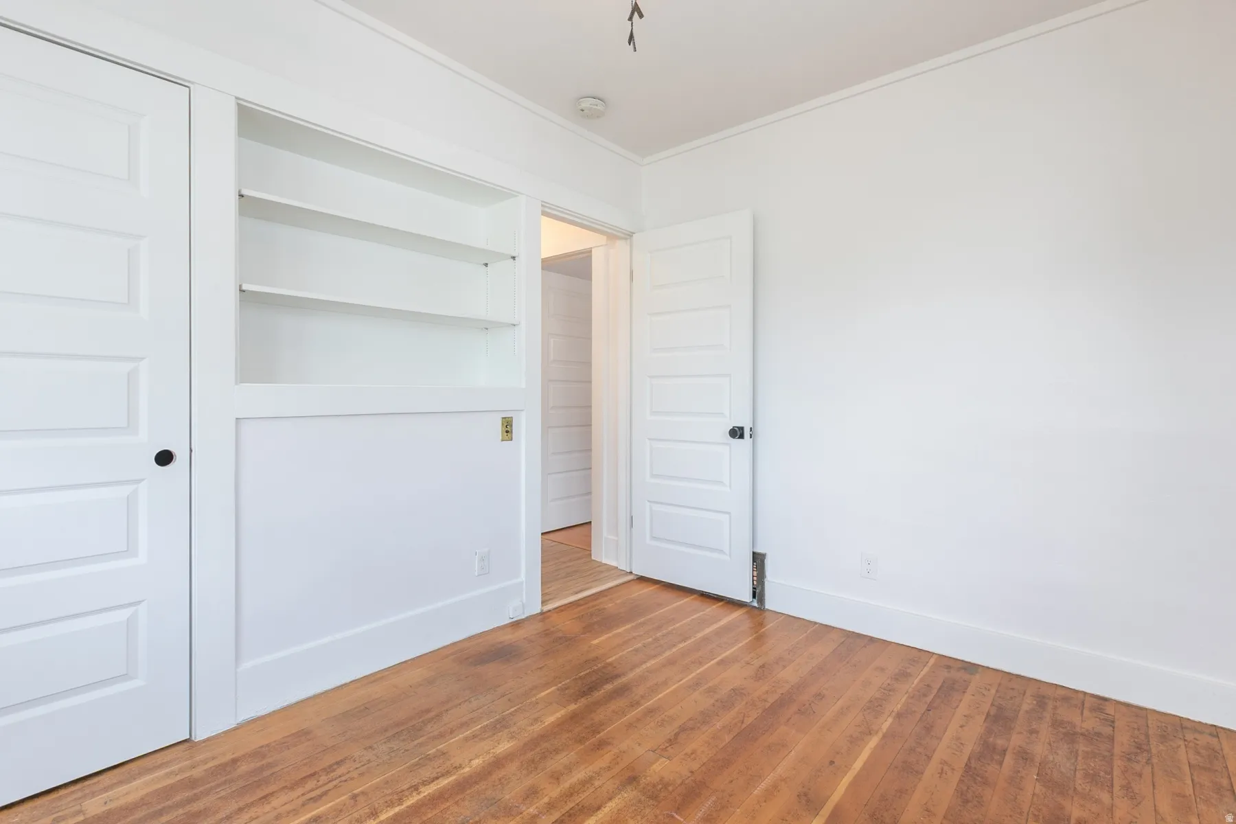 Wood-finish flooring, built-in shelving, white paneled doors, and white walls