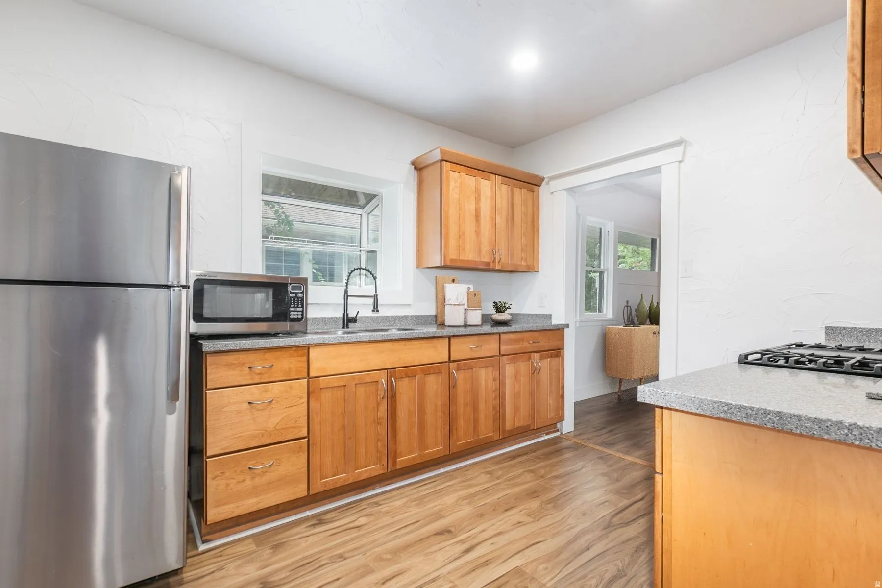 Kitchen featuring wood cabinetry, stainless steel appliances, speckled countertops, and wood-finish flooring