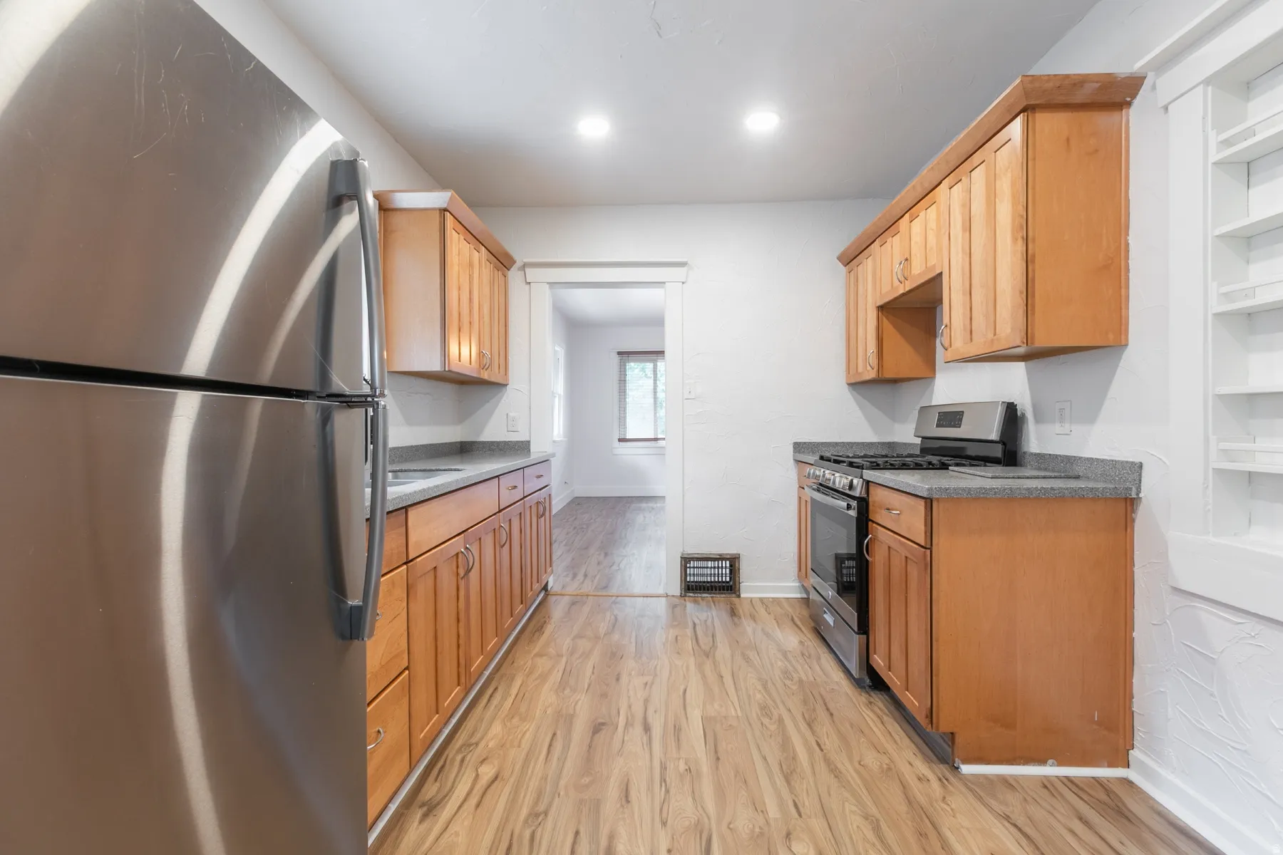 Galley kitchen featuring wood-finish flooring, full-height cabinetry, stainless steel appliances, recessed lighting, and solid surface countertops