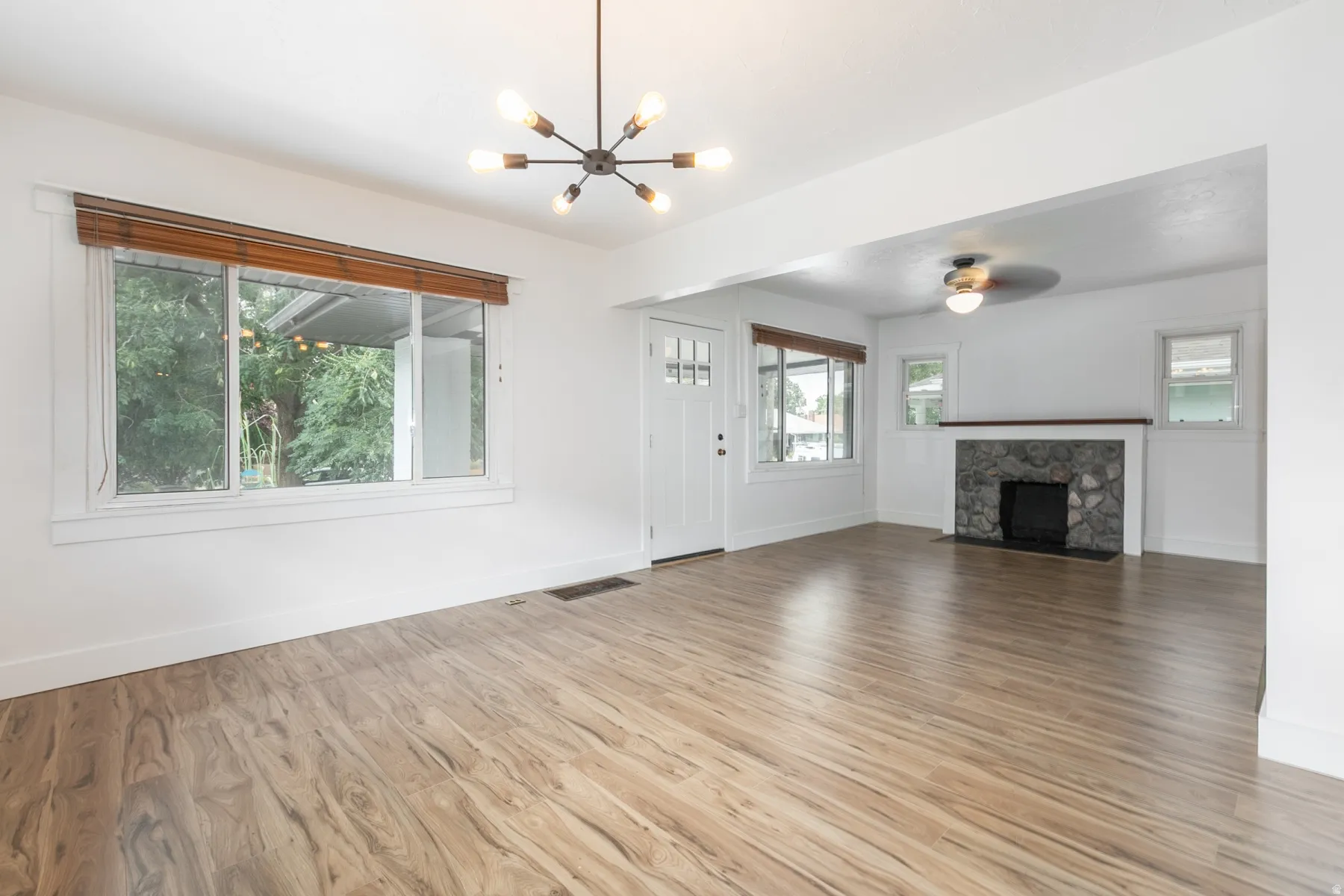 Open concept living space featuring wood-finish flooring, a contemporary chandelier, a stone-faced fireplace, and multiple windows