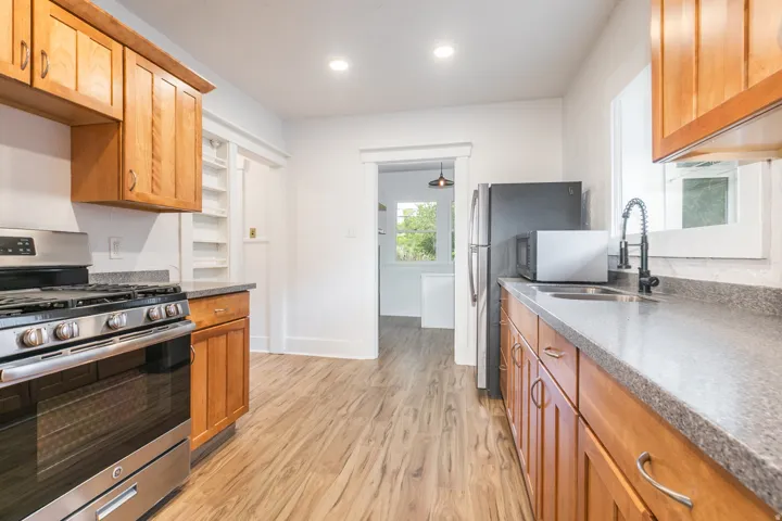 Wood-finish flooring, recessed lighting, wood cabinetry, stainless steel range, and a stainless steel sink with a matte black faucet
