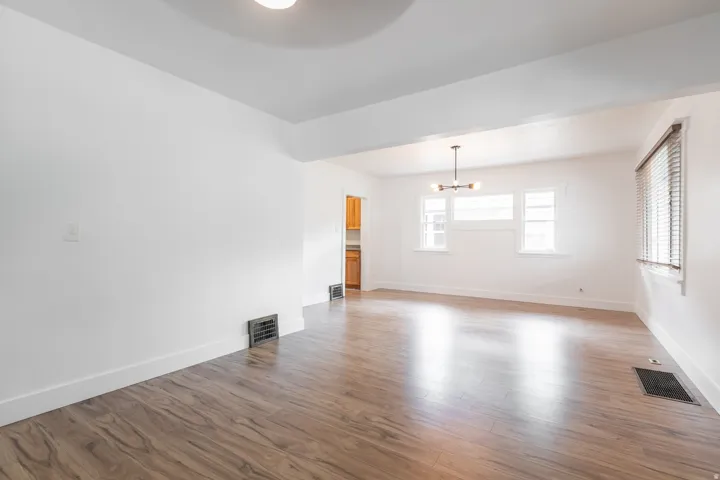 Spacious room with wood-finish flooring, white walls, and multiple windows with blinds