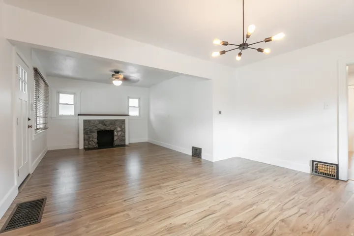 Wood-finish flooring throughout, stone fireplace with a wood mantel, modern black chandelier, and a ceiling fan