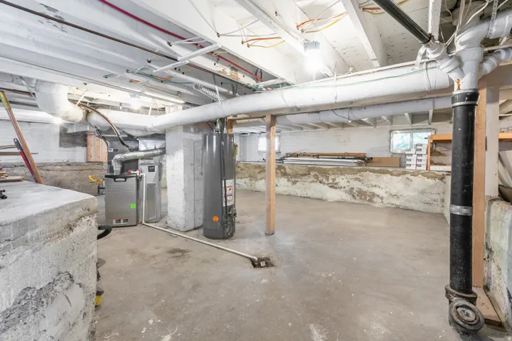Basement featuring exposed ceiling joists, concrete flooring, a water heater, and a furnace