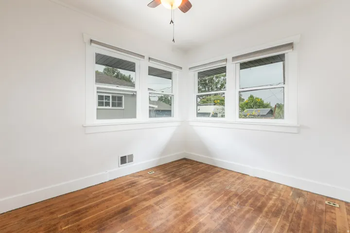 Hardwood flooring, corner window configuration, white trim, white walls, ceiling fan