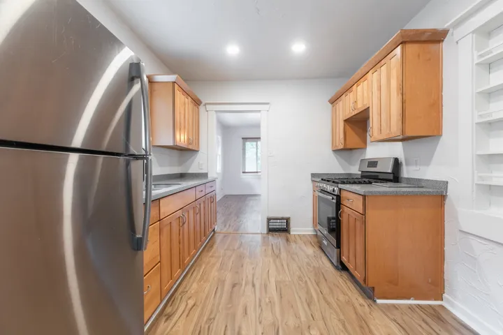 Galley kitchen featuring wood-finish flooring, full-height cabinetry, stainless steel appliances, recessed lighting, and solid surface countertops
