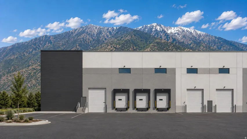 Commercial building with a mountain backdrop, featuring multiple roll-up doors, dock levelers, and an asphalt parking area