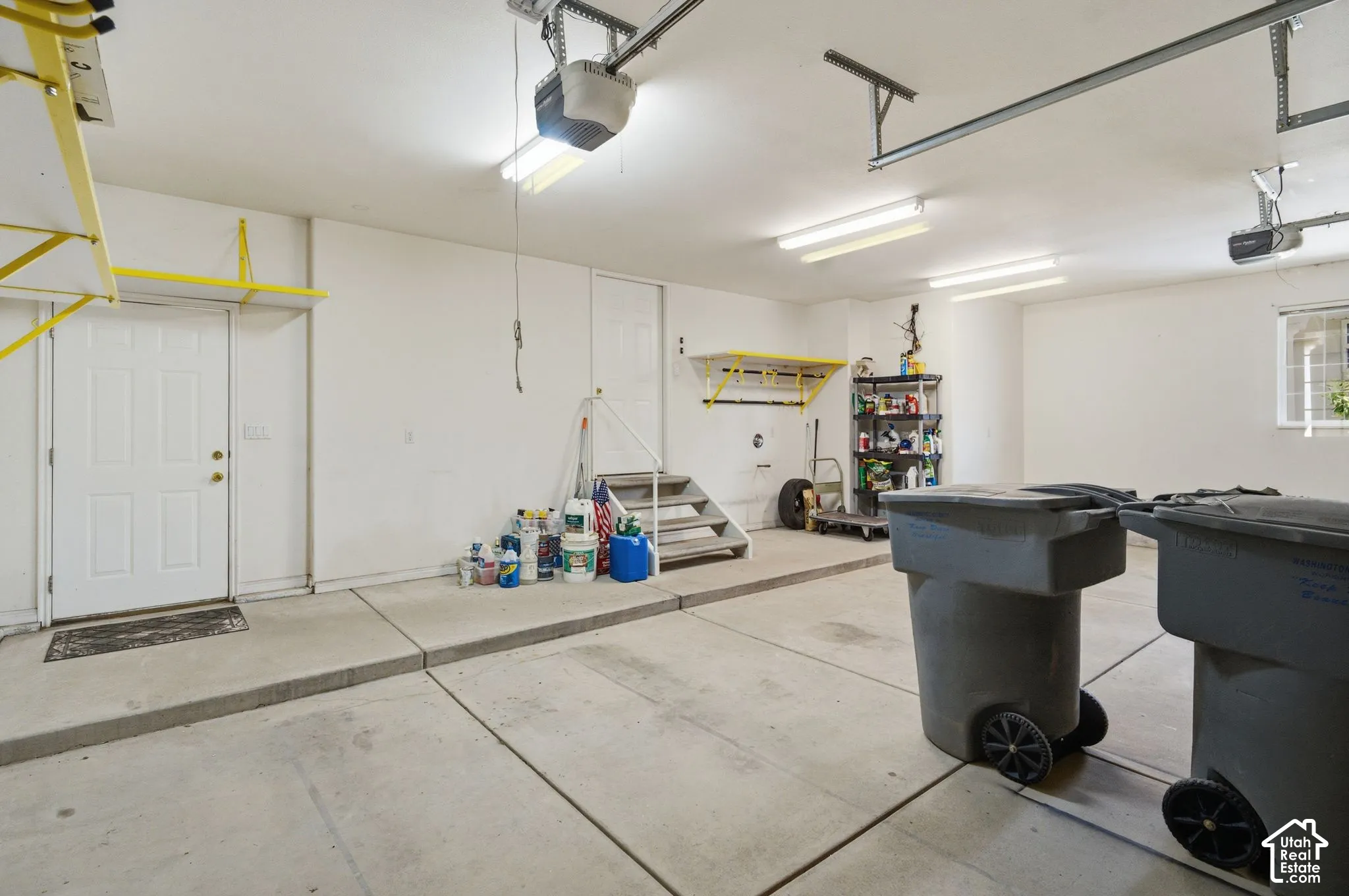 Attached two-car garage with concrete flooring, multiple overhead fluorescent light fixtures, and an automatic garage door opener