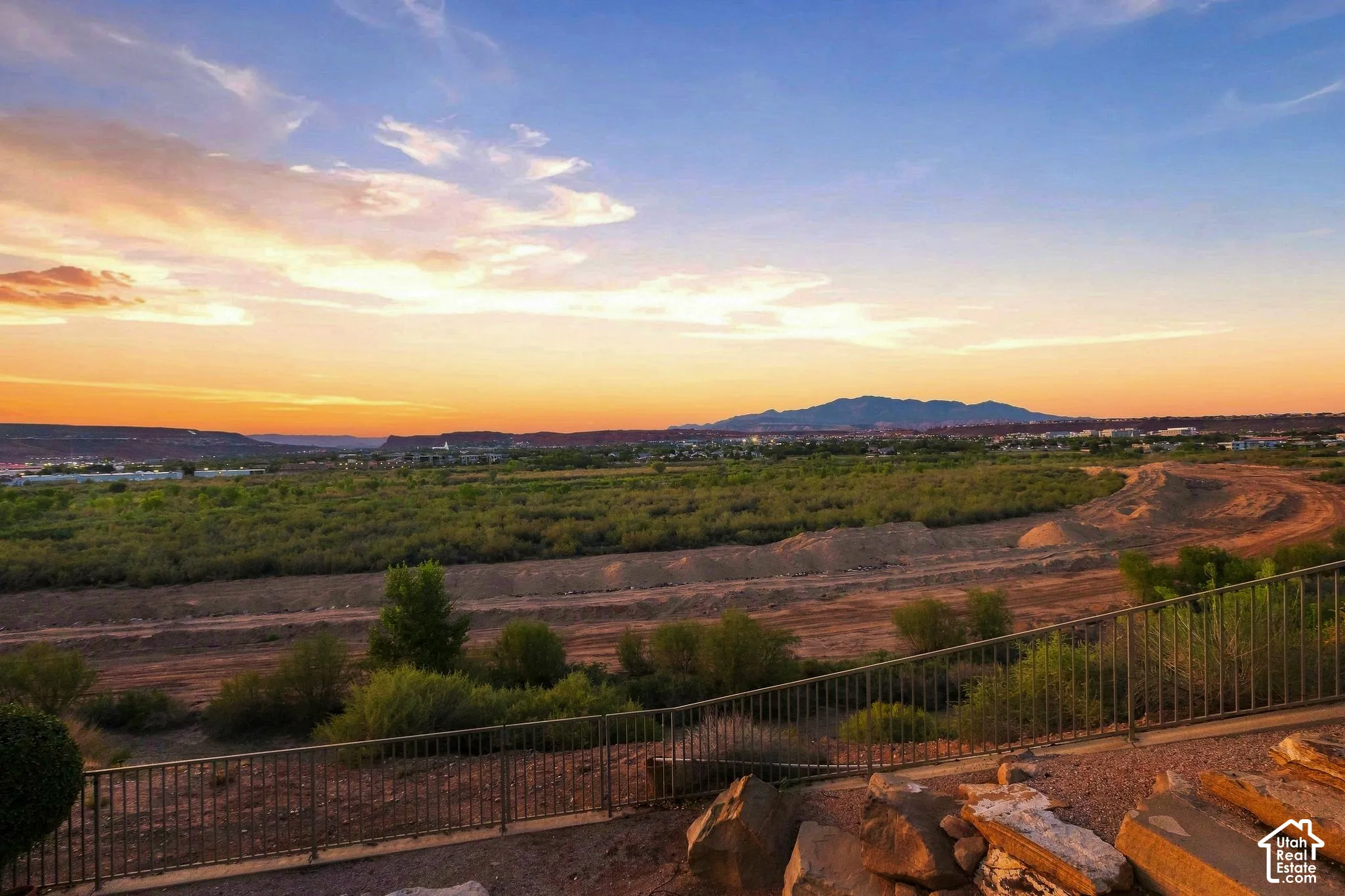 Expansive desert landscape with distant mountains, mature low-lying vegetation, and a metal perimeter fence