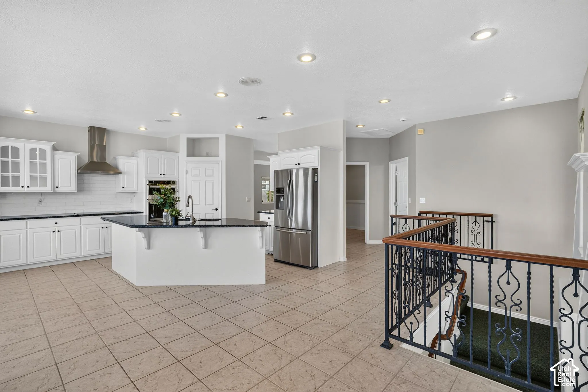 White cabinetry with dark countertops, stainless steel appliances, tile flooring, recessed lighting, and ornate metal stair railings with wood handrails