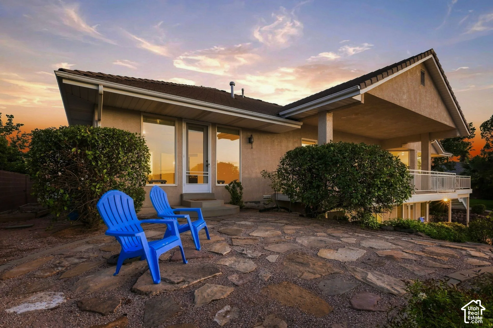 Exterior stucco finish, prominent gabled roof, flagstone patio, covered balcony, and mature landscaping