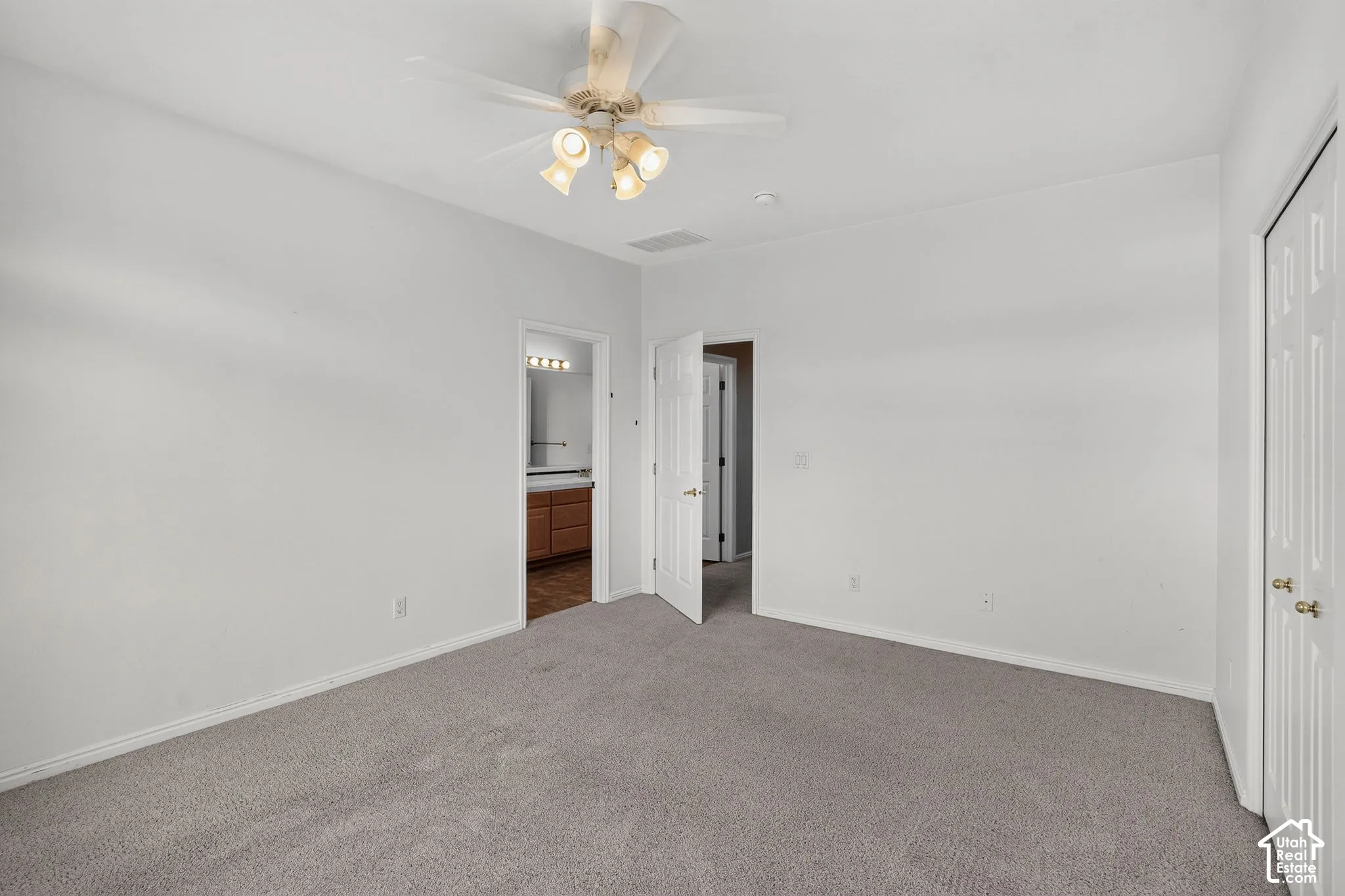 Spacious bedroom with neutral carpet flooring, ceiling fan with integrated lighting, and multiple closet access points