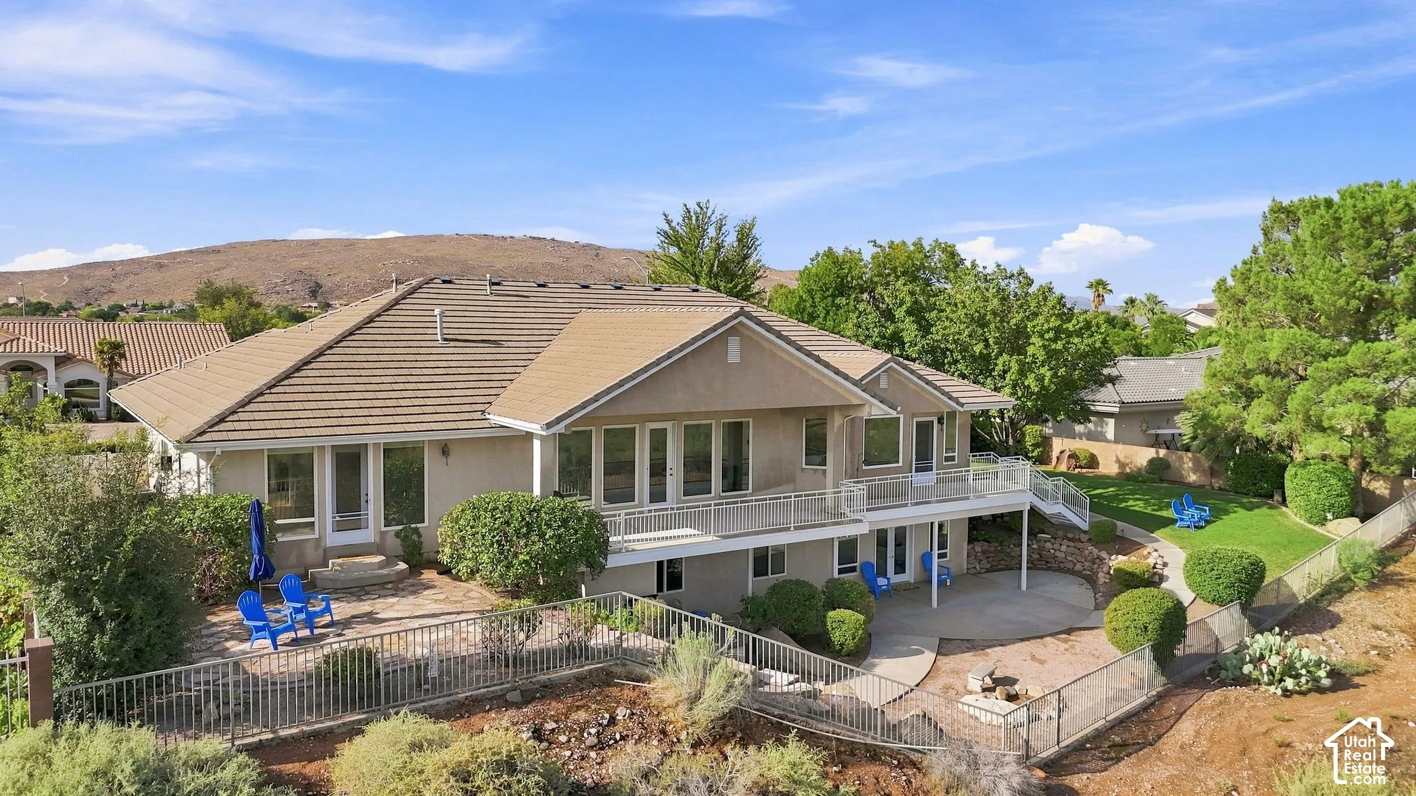 Terracotta tile roof, multiple outdoor patios, upper-level balcony with white railings, and a terraced landscaped yard